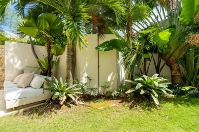 a couch in a garden with palm trees and grass at 2 bedroom villa with large garden and near Canggu in Kerobokan