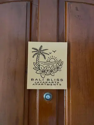 a sign on a wooden door with a beach and palm trees at Bali Bliss Jayakarta Apartments in Seminyak