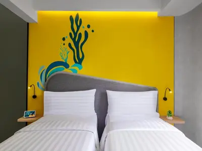 two beds in a room with a yellow wall at Quest Vibe Dewi Sri Bali in Legian