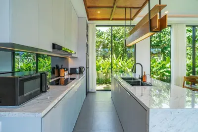 a kitchen with white countertops and large windows at Bedawang, Exquisite Seminyak 4BR Villa with Huge Pool in Seminyak