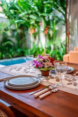 a wooden table with plates and glasses and flowers on it at Villa Boha Seminyak in Seminyak