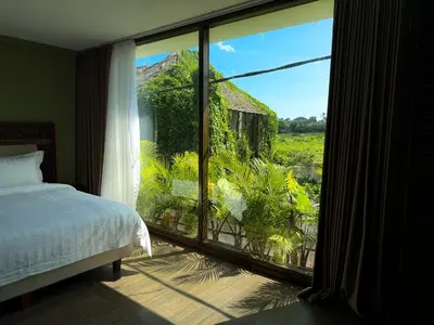 a bedroom with a large window with a view of a yard at Ducat Living in Canggu