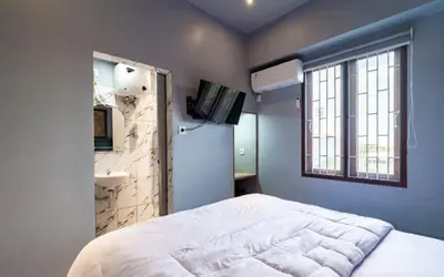 a bedroom with a white bed and a bathroom at Hotel Dakozi Living in Kuta