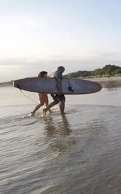 two people walking on the beach with a surfboard at Villa Anyelir in Seminyak