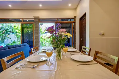 a table with plates and glasses and a vase of flowers at Seminyak Happy Villa in Legian
