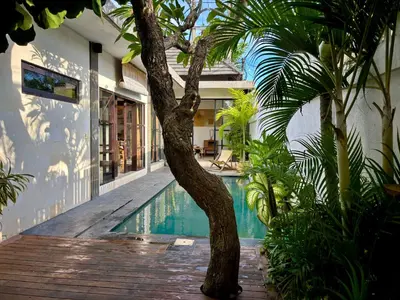 a swimming pool next to a house with a palm tree at Villa Omarama Seminyak Beach in Seminyak