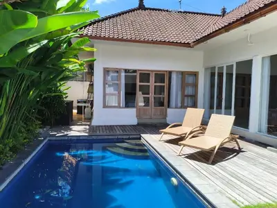 a pool with two chairs and a house at Villa Videl in Seminyak