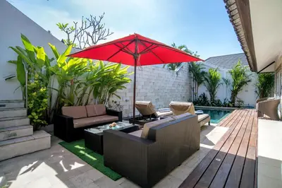 a patio with a red umbrella and chairs and a pool at Villa Kazari Zen in Seminyak