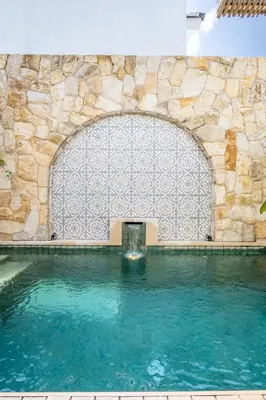 a swimming pool with a stone wall and a fountain at Villa Monstera A7 By Aishwarya International in Kerobokan