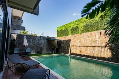 a swimming pool with two chairs and an umbrella at Villa Maya in Kerobokan