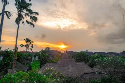 a sunset over a building and palm trees at D'House Seminyak in Seminyak