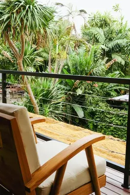 a wooden chair sitting on a balcony with palm trees at Villa Frankie in Central Legian in Legian