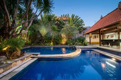a swimming pool in a backyard with trees and a house at Sandy Shores Bali in Seminyak