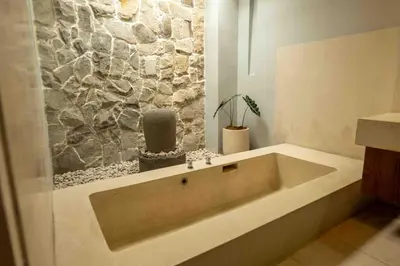a large bath tub in a bathroom with a stone wall at Tuluscolivingseminyakvilla1 in Seminyak