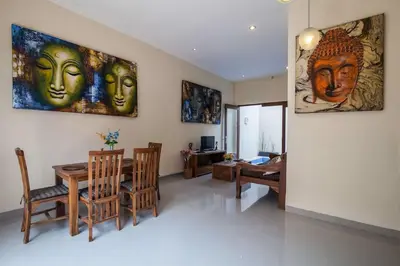a living room with a table and chairs and paintings on the wall at The Lavana Villa De Kerobokan in Seminyak