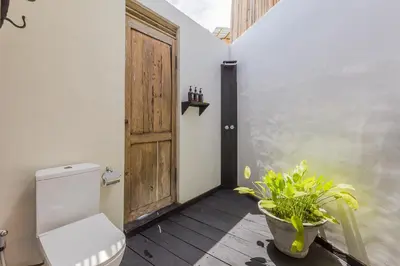 a bathroom with a toilet and a wooden door at Villa Ubuntu 3BR Pool Ricefield Family&Friends group near Canggu in Kerobokan