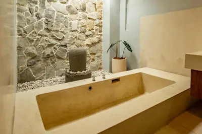 a large tub in a bathroom with a stone wall at tuluscolivingseminyakvilla2 in Seminyak
