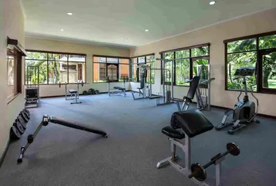 a gym with several exercise equipment in a room with windows at Mana Suites Bali in Kuta