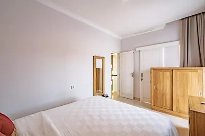 a white bedroom with a bed and a wooden cabinet at Casa Raya 4BR Villa in Kuta in Kuta