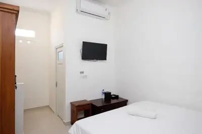 a white bedroom with a bed and a tv on the wall at Urbanview Hotel Arta Guna Casa in Kerobokan