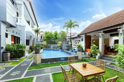 a backyard with a wooden table and chairs and a swimming pool at Cove De Pavilla in Sanur