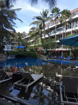 a pool at a resort with chairs and palm trees at Cozy Apartement in Seminyak in Uluwatu
