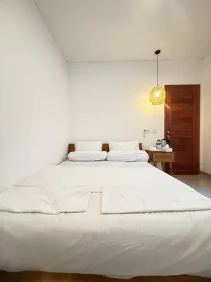 a large white bed in a white bedroom with a lamp at Home Stay Room in Bali Near Sanur Beach in Sanur