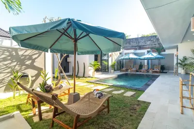 a patio with chairs and an umbrella and a pool at Villa Vela 1 - Brand new 3 bedroom villa in Seminyak