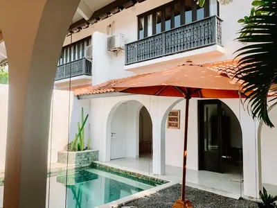 an umbrella in front of a house with a swimming pool at Lovely 2 Bedroom Pool Villa Close to The Beach in Seminyak