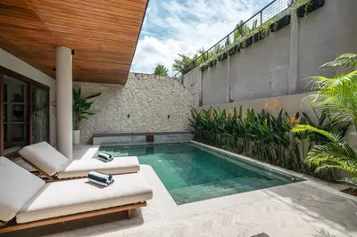 a swimming pool in a backyard with two chairs and aitating at Sonaa Villa Bali in Canggu