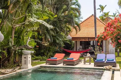 a pool with chairs and a hammock next to a house at Seminyak Most Wanted Villa for family vacation in Seminyak