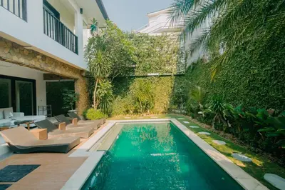 a swimming pool in a garden with chairs and a wall at Villa C31 Seminyak in Seminyak