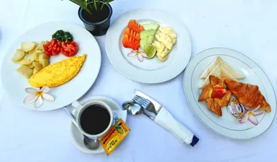 a table with three plates of food and a cup of coffee at Srikandi Inn in Jimbaran