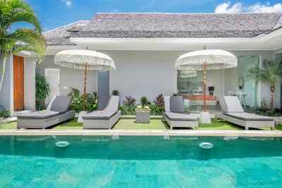 a pool with chairs and umbrellas next to a house at Villa Shankara 1 in Canggu