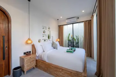 a bedroom with a large white bed and a window at La Vilaya Villa in Kerobokan