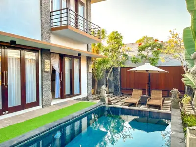 a house with a swimming pool with chairs and an umbrella at Ratu Deandra Villa Seminyak in Seminyak