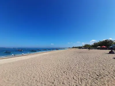 a sandy beach with people in the ocean on a clear day at ABI Hotel3 - 1 minute to the Beach and 1 second to the Mall in Ngurah Rai International Airport