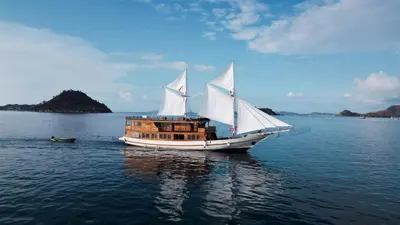 a boat with white sails in the water at Boat Komodo in Seminyak