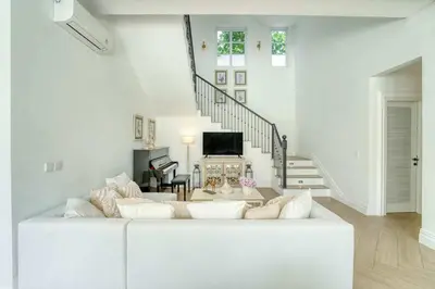 a white living room with a white couch and stairs at Colonial House 4BR Villa With Ocean View in Berawa in Canggu