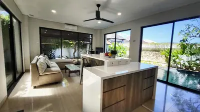 a kitchen with a living room with glass windows at Villa Lans By Baliem Villa in Jimbaran