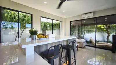 a kitchen with a counter and some chairs and windows at Villa Lans By Baliem Villa in Jimbaran