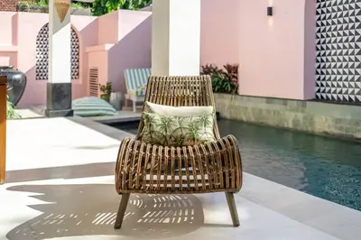 a wicker chair with a pillow sitting next to a pool at Ocean Two 1BR Villa Honeymoon Seminyak in Seminyak