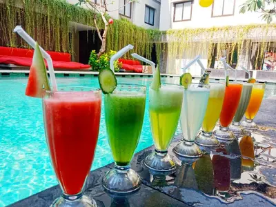 a row of different colored drinks in wine glasses next to a swimming pool at Savvoya Hotel Seminyak in Seminyak