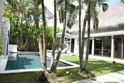 a pool with palm trees in front of a house at Casa Veluna - Seminyak in Seminyak