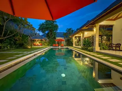 a swimming pool with an umbrella next to a house at Luxury 4BR - Villa Santai - Central Seminyak in Seminyak
