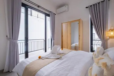 a bedroom with a large white bed with a large window at La Casa Gomes in Nusa Dua