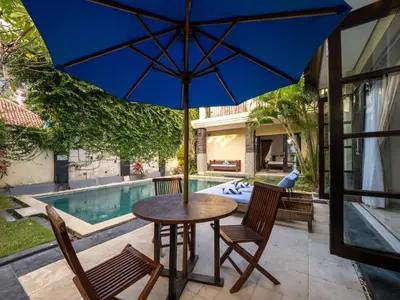 a table and chairs with an umbrella next to a swimming pool at Villa Cometa Prime Seminyak by Adam Jyota Management in Seminyak