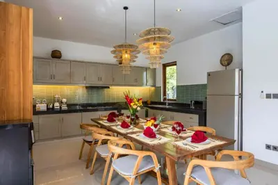 a kitchen with a table with chairs and a refrigerator at Erianthe Peaceful 3 BR Private Pool Villa in Kerobokan