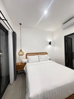 a white bedroom with a large bed and a nightstand at Della Solea Seminyak in Seminyak
