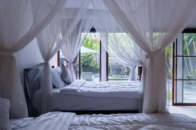 two beds in a bedroom with white drapes at Karen's Tropical Villa in Seminyak